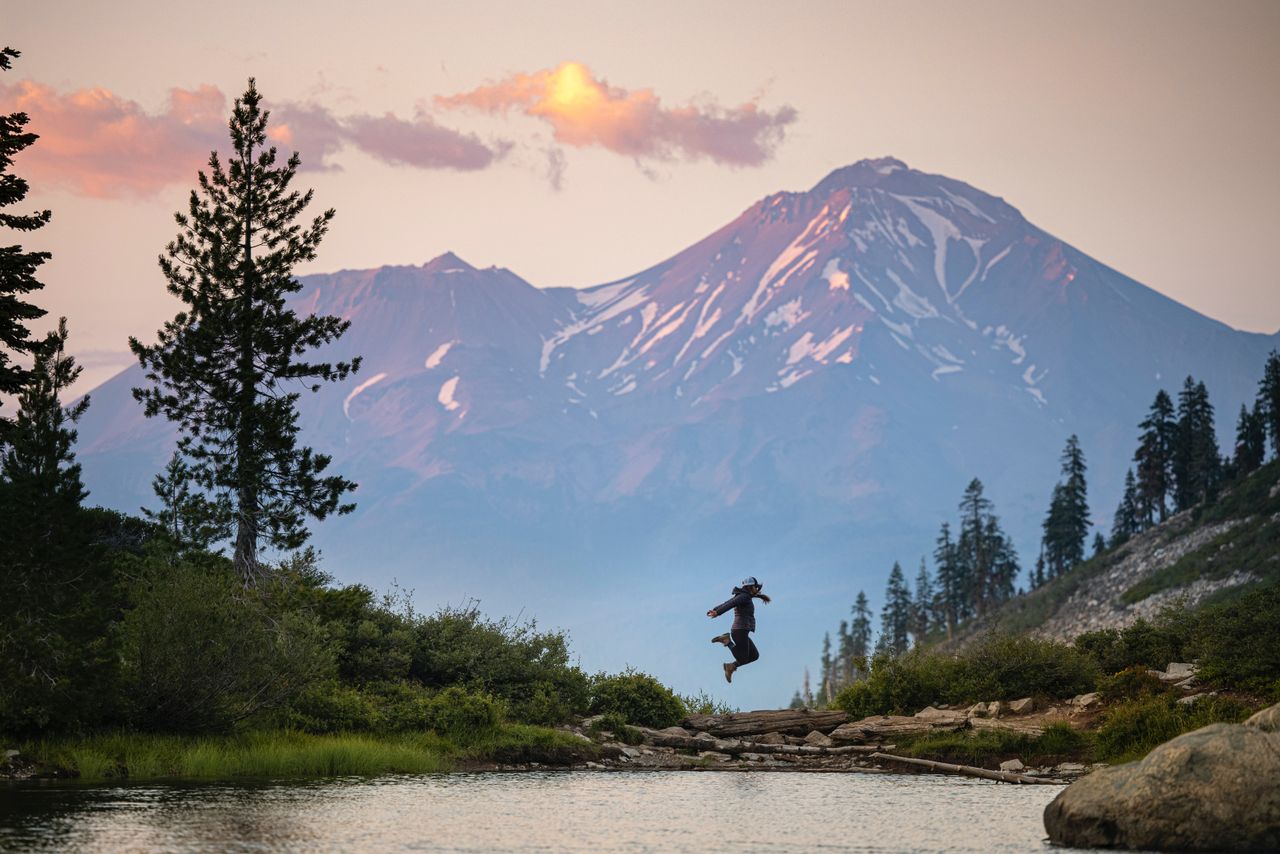 A person leaps joyfully in front of a scenic mountain during a beautiful evening.