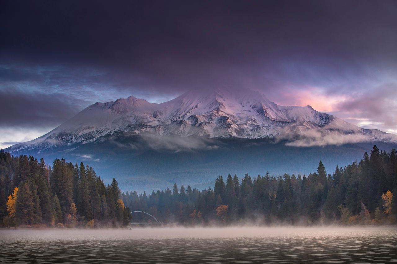 Captivating view of Mount Shasta with a misty forest foreground and dramatic clouds at twilight.
