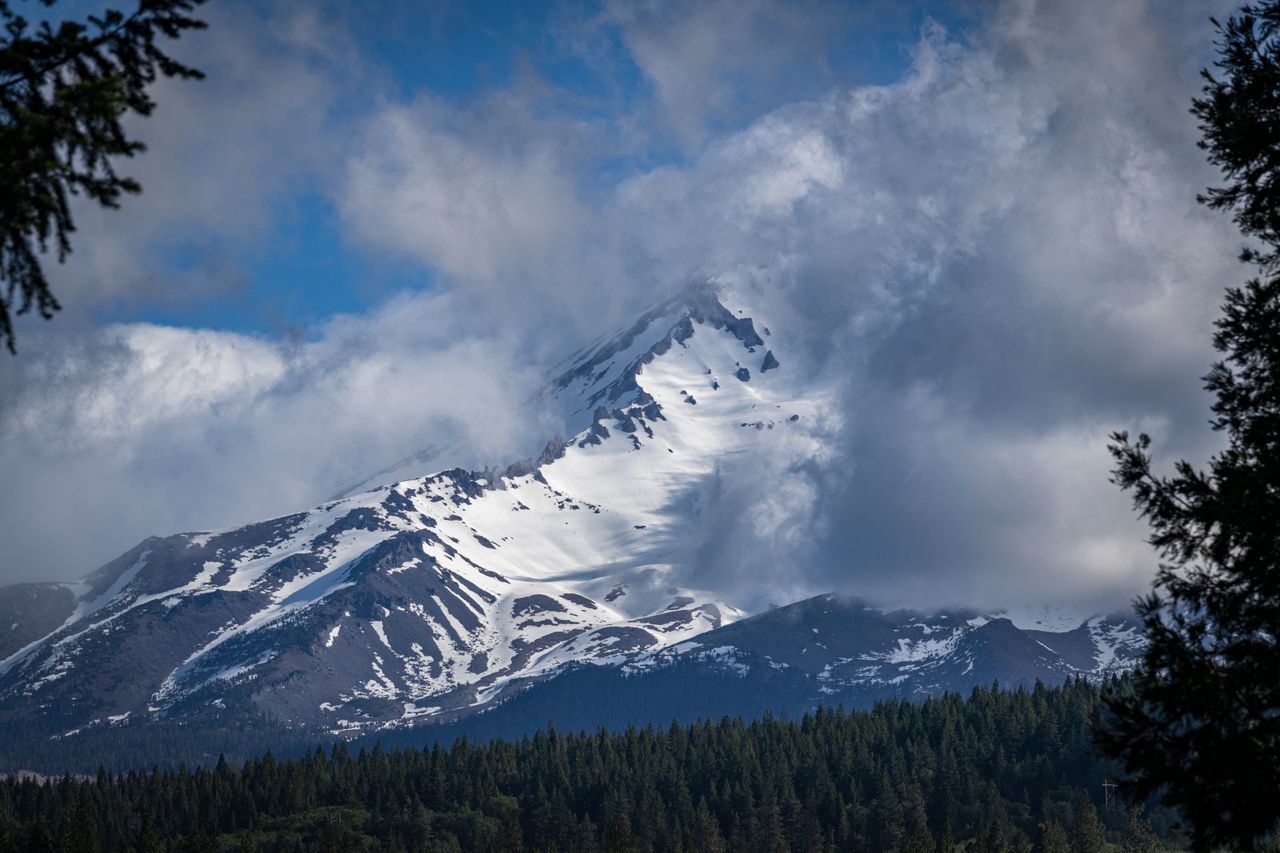 Stunning view of a snow-capped mountain peak partially covered by clouds, surrounded by evergreen forest.